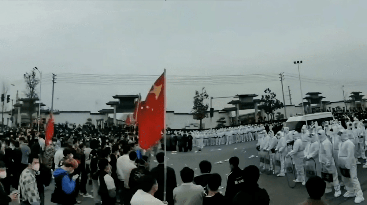 Foxconn workers holding Chinese national flags during the November 2022 protest at the Zhengzhou plant, with local police present.