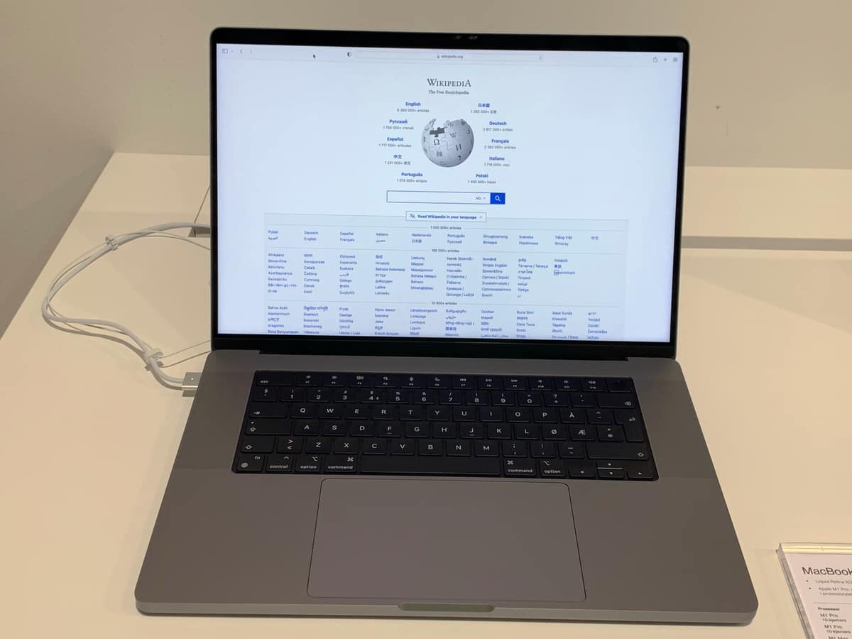 A 16-inch MacBook Pro (M1 Pro, 2021) open on a desk, displaying the Wikipedia main page on its Liquid Retina XDR display.