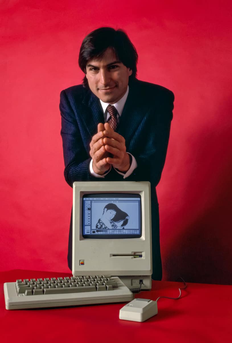 Steve Jobs standing beside an original Macintosh computer in January 1984